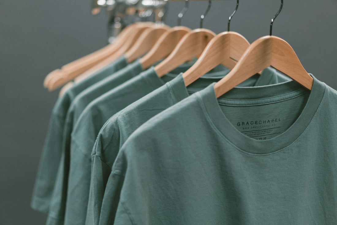 Reihe schlichter Shirts auf Holzbügeln vor ruhigem Hintergrund